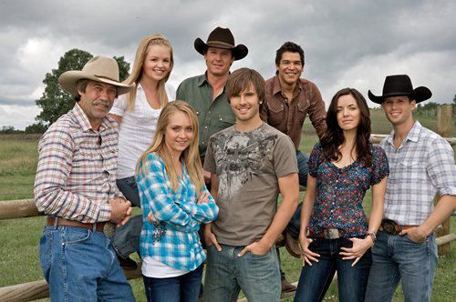 The cast of Heartland gathers for a photo on the ranch, smiling and looking towards the horizon.