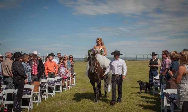 Amber Marshall and Shawn Turner on horseback, dressed in wedding attire, with a rustic ranch backdrop